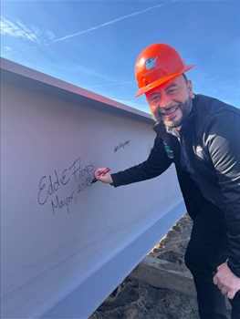Mayor Eddie in a hard hat signing his name on a beam at the new pool
